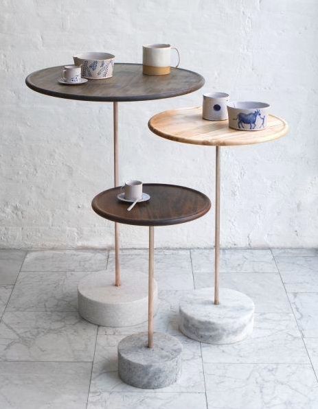 Three round wood tops on wooden stems over white marble bases.