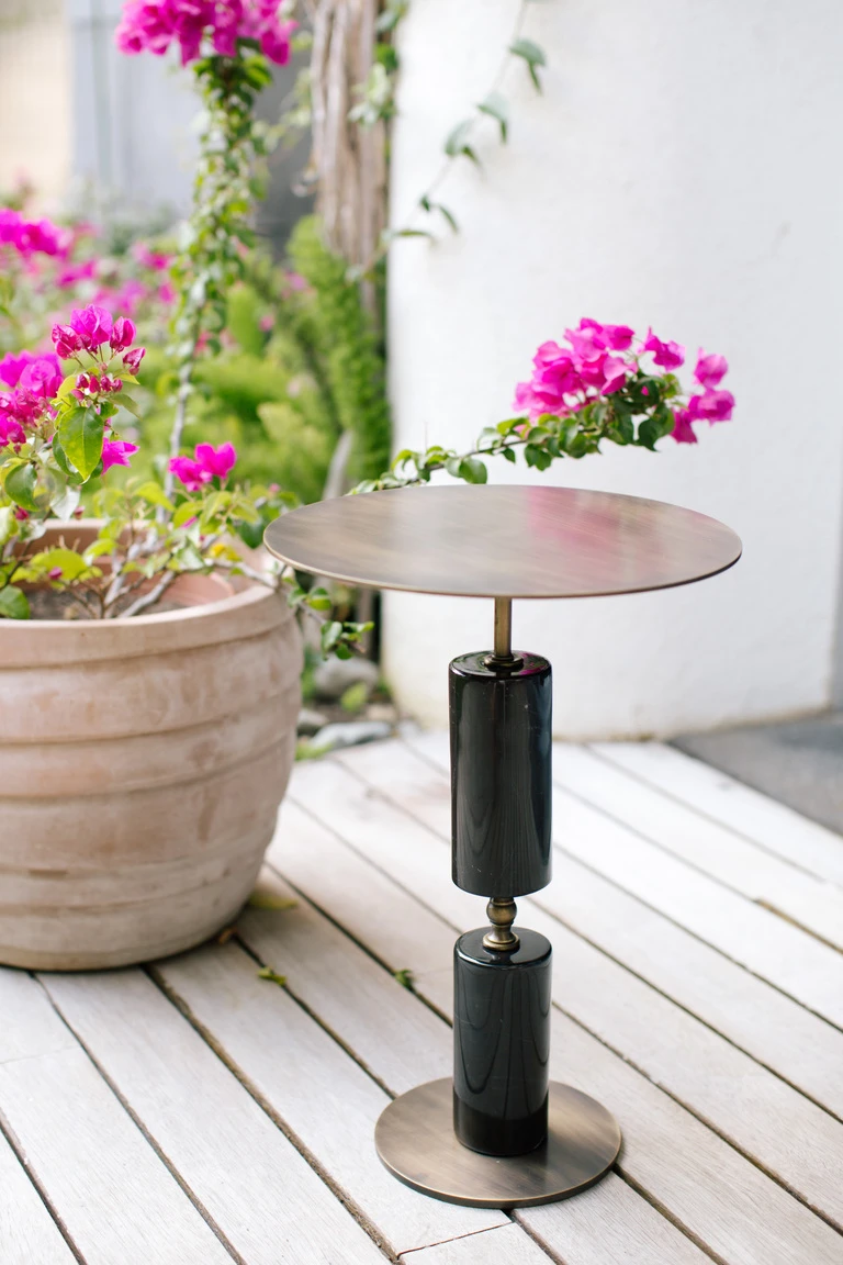 A side table with a bronze round top over two black marble cylinders.